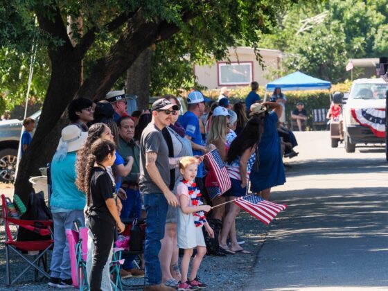 Families line the parade route in downtown Grimes, waving American flags as parade entries pass during the community's 175th anniversary celebration on July 4. Photo by Chris Pedigo.